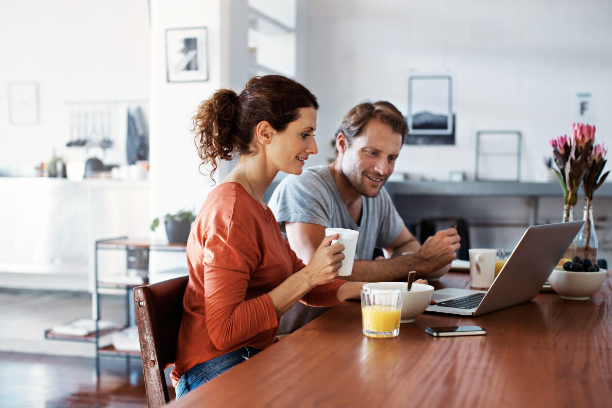 Couple eating breakfast while reading on their laptop
