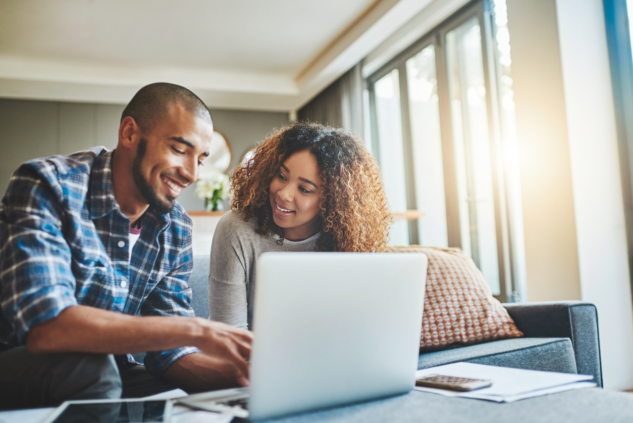 A couple smiling at each other while the male types on his laptop