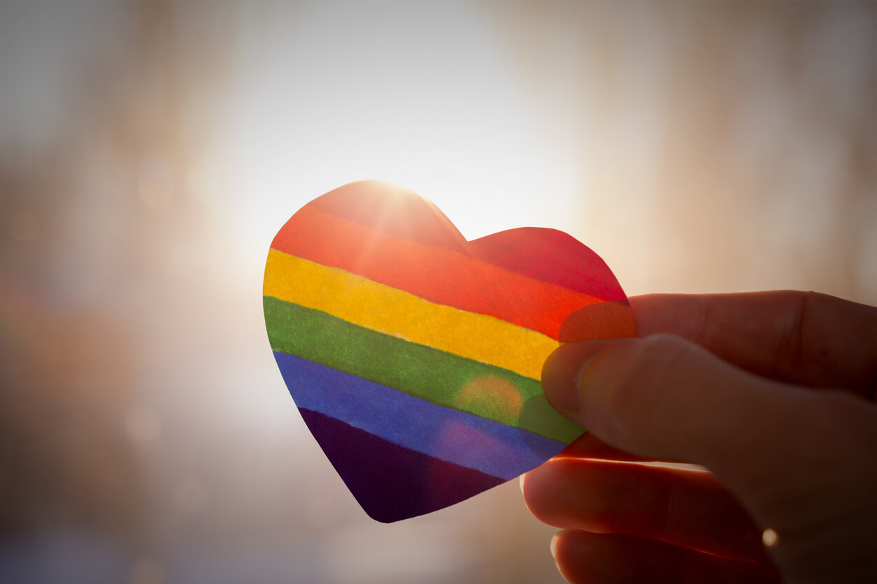 Person holding a paper cutout of a rainbow colored heart