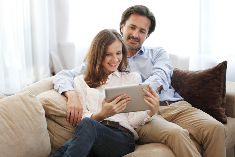 A couple lying on the couch and viewing their tablet