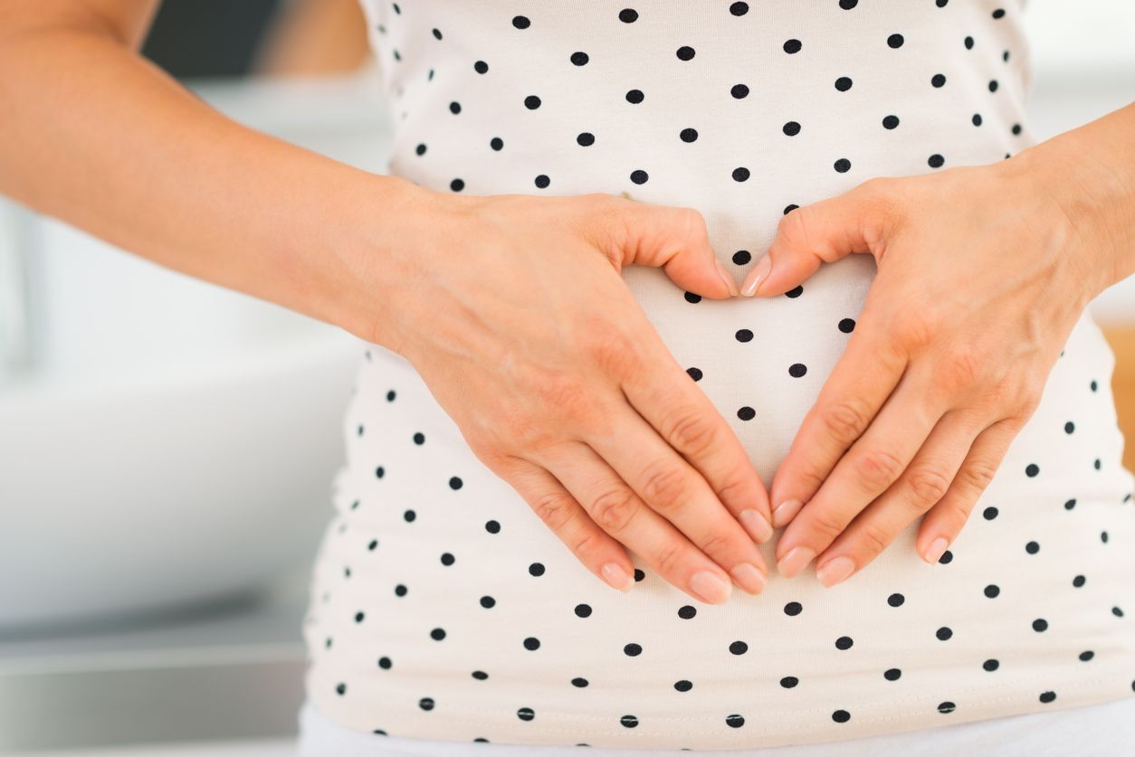 A female with a polka dot dress holding her stomach while making a heart sign