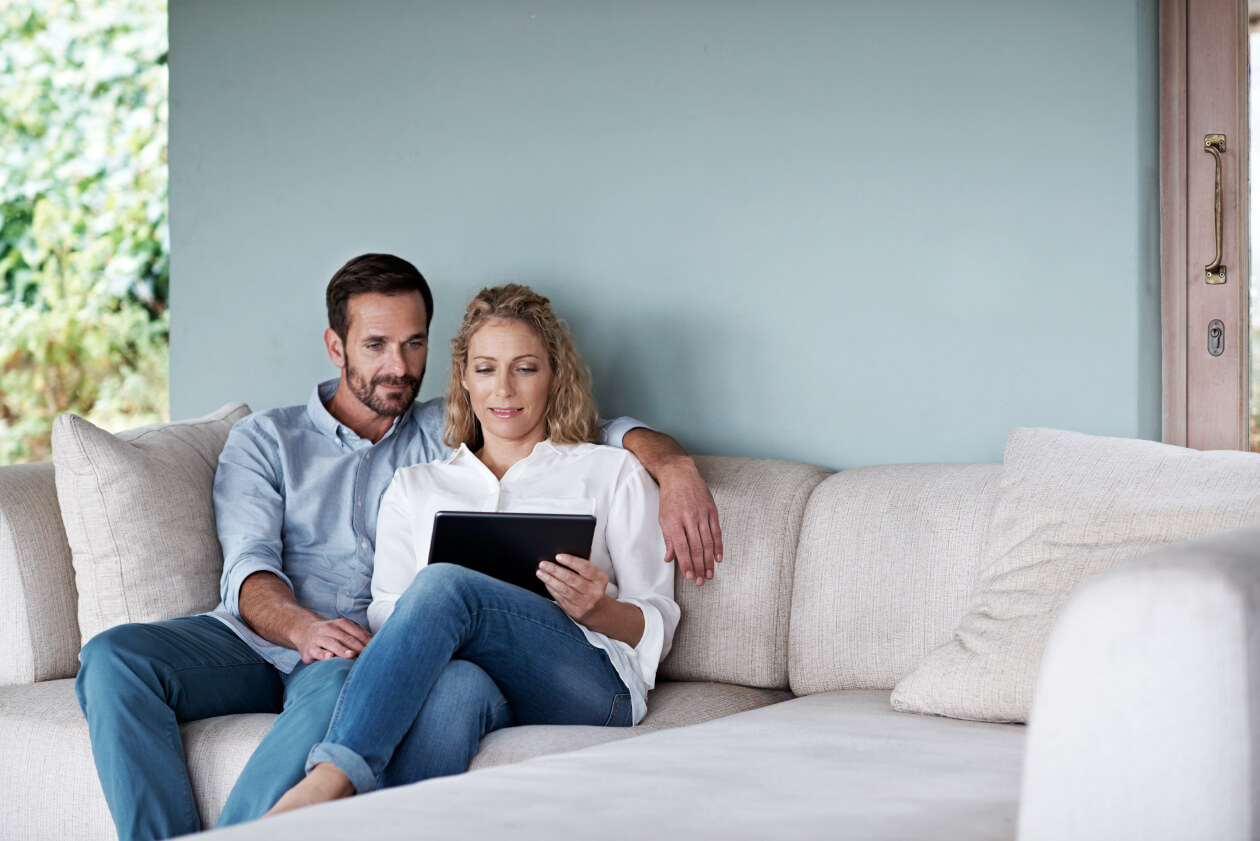 A couple setting on a couch while going reading on their tablet