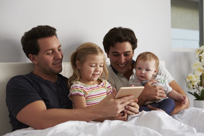 an LGBTQ couple holding their children while in bed
