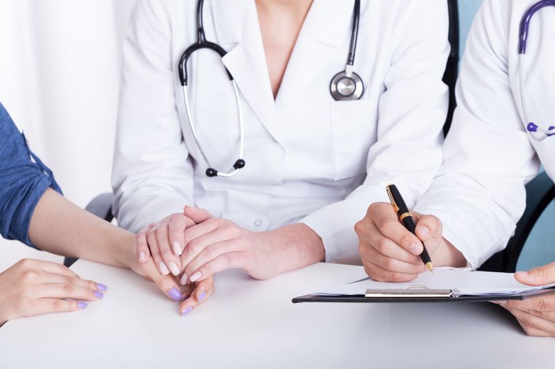 female doctor holding a patient's hand while a nurse records notes