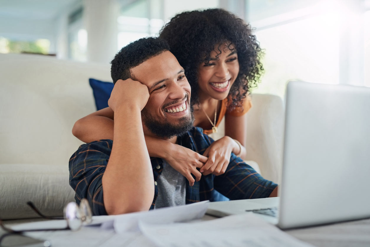 A couple smiling together while viewing their laptop