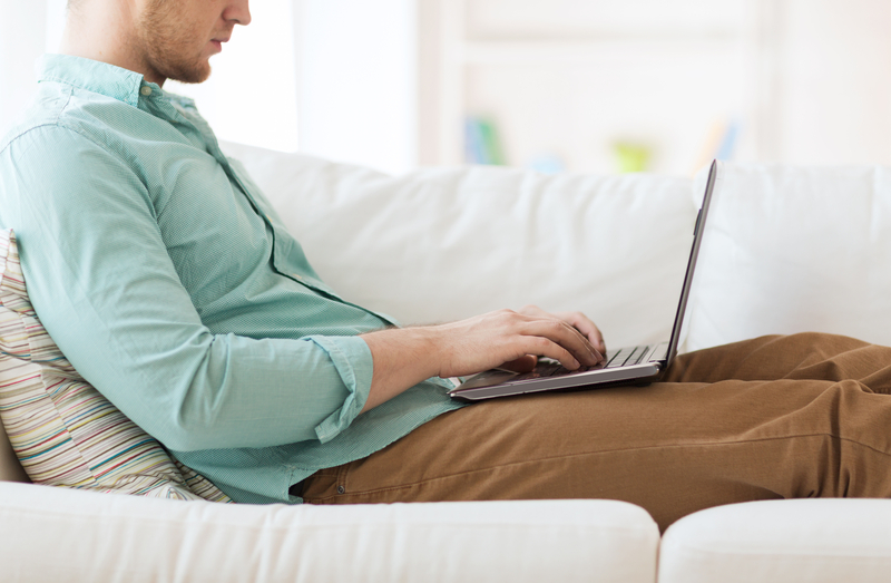Man typing on his laptop while lying on a couch